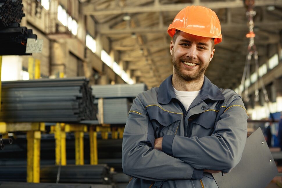 A steel industry worker smiling in front of a warehouse